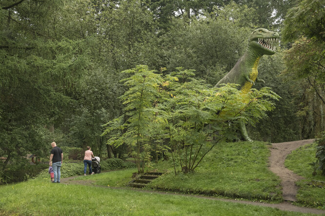 Das Modell eines Dinosauriers auf einem Hügel im Grünen