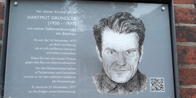 Eine Gedenktafel für Hartmut Gründler mit seinem Porträt und Lebenslauf hängt an einer roten Backsteinwand
