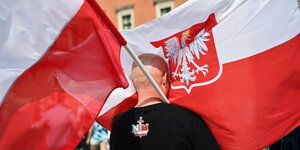 Ein Mann steht zwischen zwei großen Polen-Flaggen.