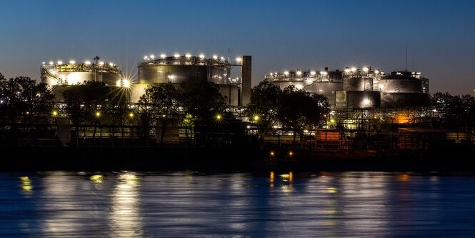 Beleuchtete Industrieanlagen der BASF in der Dämmerung, der Rhein ist im Vordergrund