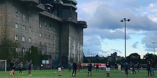 Frauen in sportkleidung stehen auf einer grünen Fläche neben einer düster-grauen Betonwand