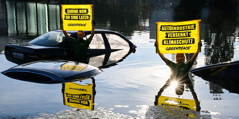 Protestaktion von Greenpeace, versunke Autos und 2 Aktivisten,die gelbe Schilder halten