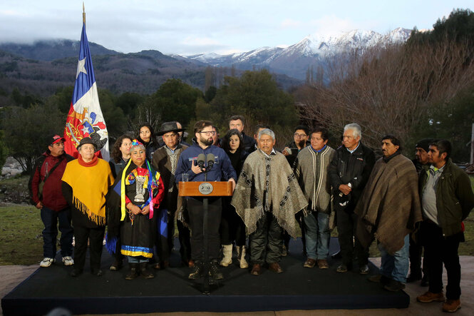 Präsident Boric vor einer Bergkulisse, umringt von traditionell gekleideten Indigenen