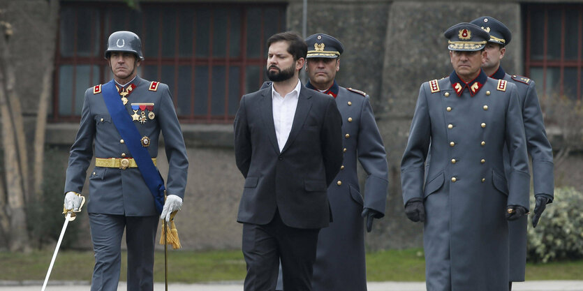 Gabriel Boric, im schwarzen Anzug, zwischen Militärs in Uniform