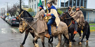 Vier Menschen auf Pferden reiten offenbar gemächlich durch eine Stadt