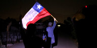 Ein Mann schwenkt bei Dunkelheit die chilenische Fahne. Er steht mit dem Rücken zur Kamera