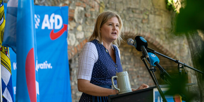 Eine Frau mit Bierseidel und blauem Dirndl vor AFD Fahnen