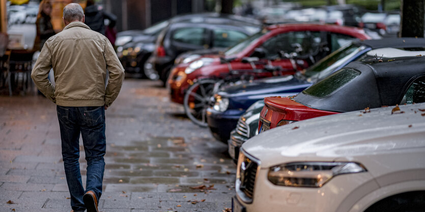 Ein Mann geht an parkenden Autos vorbei