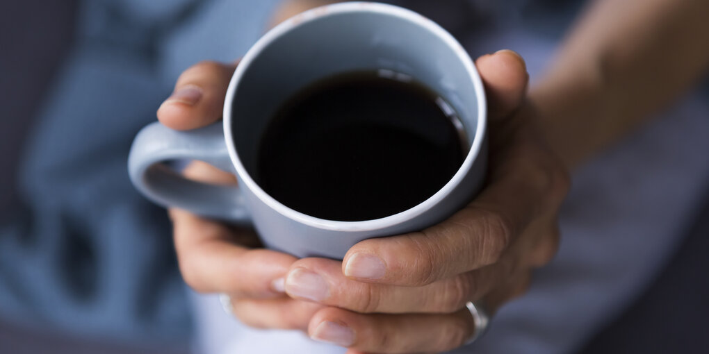 Eine Frauenhand hält eine blaue Kaffeetasse