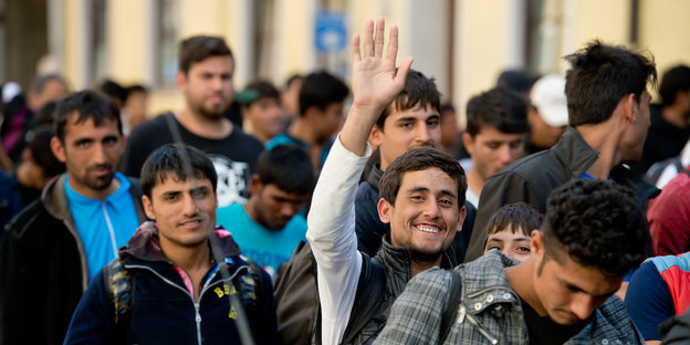 Winkender Mann in einer Gruppe von Flüchtlingen.