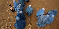 Fraun in blauen Burkas hocken auf sandigem Boden