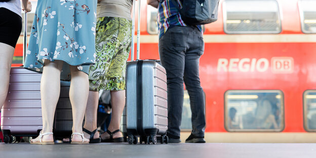 Menschen mit Koffern stehen an einem Bahnsteig vor einem Regionalexpress