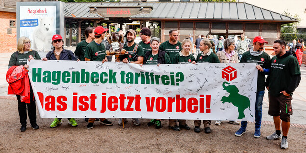 Mitarbeiter des Tierparks Hagenbeck halten vor dem Eingang ein Banner mit der Aufschrift "Hagenbeck tariffrei? Das ist jetzt vorbei!" in den Händen.
