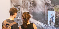 Zwei Personen stehen vor Fotografien, die Zerstörung zeigen