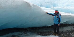 Ein Mann in blauer Jacke steht vor einer Eiswand.