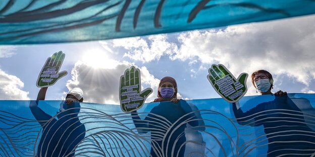 Drei Menschen protestieren mit großen Händen aus Pappe beim Klimastreik in Manila