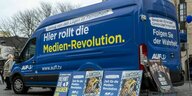 ein blauer Lieferwagen von AUF1 mit der Aufschrift: Hier rollte die Medien-Revolution - Folgen Sie der Wahrheit . Am Lieferwagen lehnen Plakate.