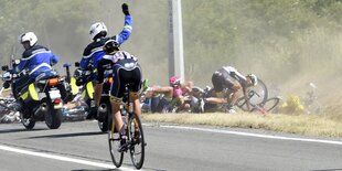 Radprofis liegen im Straßengraben, neben ihnen fahren Motorräder