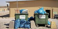 Zwei überquellende Müllcontainer mit dem Firmennamen Ecolog stehen vor einer Baracke.
