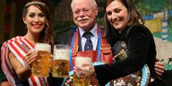Ulrich Mäurer stößt beim Freimarkt mit zwei jungen Frauen an: Jede der Personen hält einen Halbliterkrug frischgezapften Biers in der Hand.