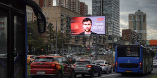 Ein Großbildschirm mit Wahlwerbung über der viel befahrenen Straße einer Metropole