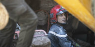 Ein Mann mit rotem Sicherheitshelm in den Trümmern eines Hauses. Er schaut nach oben.