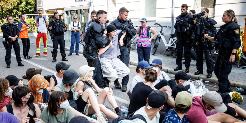 Zwei Polizisten zerren einen jungen Menschen weg