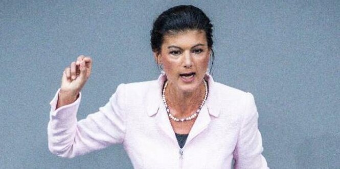 Sahra Wagenknecht in weißem Sakko steht an einem rednerpult und gestikuliert