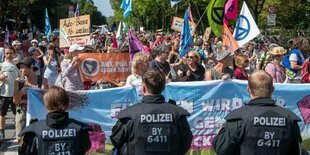 Drei Polizist:innen sind von hinten zu sehen. Sie blockieren den Protest von Klimaaktivisten auf der IAA