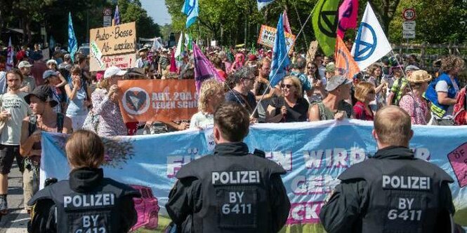 Drei Polizist:innen sind von hinten zu sehen. Sie blockieren den Protest von Klimaaktivisten auf der IAA