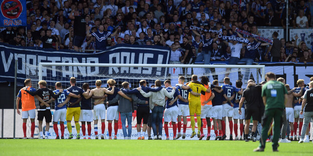 Kiels spieler feiern nach dem Spiel gegen Paderborn mit den Fans. In der Fankurve hängt ein Banner mit der Aufschrift "Vorstand raus".