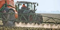 Traktor zieht eine Pestizidspritze über ein Feld, aus der eine Flüssigkeit gespritzt wird