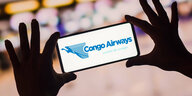 Hände halten ein Smartphone das ein Congo Airways Logo zeigt.