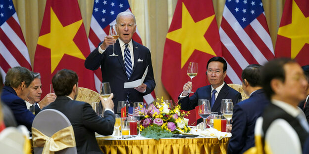 Präsident Biden und Präsident Vo Van Thuong halten Weingläser in der Hand und sitzen an einem runden Tisch.