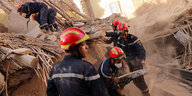Männer in blauen Schutzanzügen und roten Helmen arbeiten in einem zerstörten Gebäude