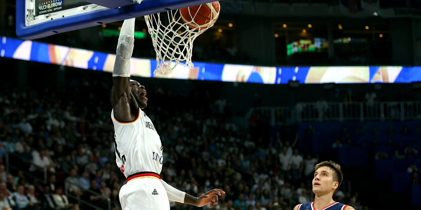 Dennis Schröder springt hoch und wirft einen Ball in den Korb, ein serbicher Gegenspieler schaut erstaunt zu