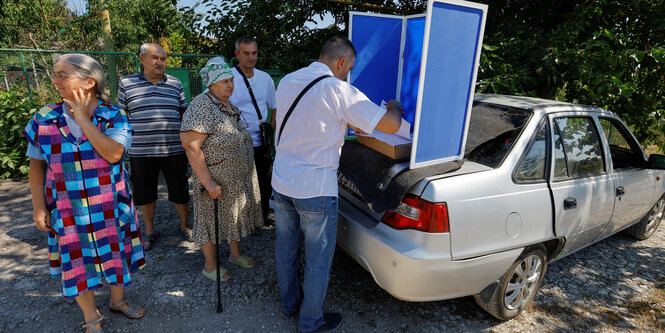 Menschen wählen an einer Wahlkabine an einem Auto.