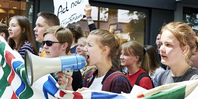 Mehrere junge Protestierende mit Megafon, Plakaten und einem Banner