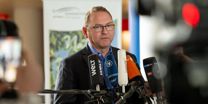 Frank Werneke, ein Mann mit kurzen Haaren und Brille, vor Mikrofonen.