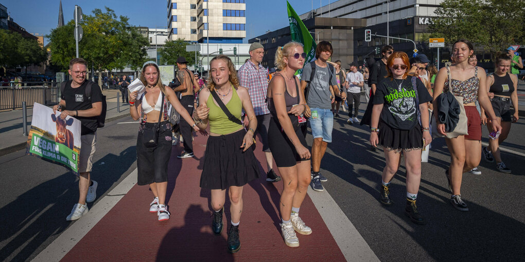 leicht bekleidete AktivistInnen gehen an einem heißen TAg tänzelnd und schwitzend über eine Strasse