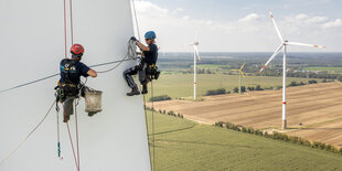 Industriekletterer beim Arbeiten am 55 Meter langen Rotorblatt einer Windkraftanlage, im Hintergrund sind in der Landschaft weitere Windkraftanlagen zu sehen