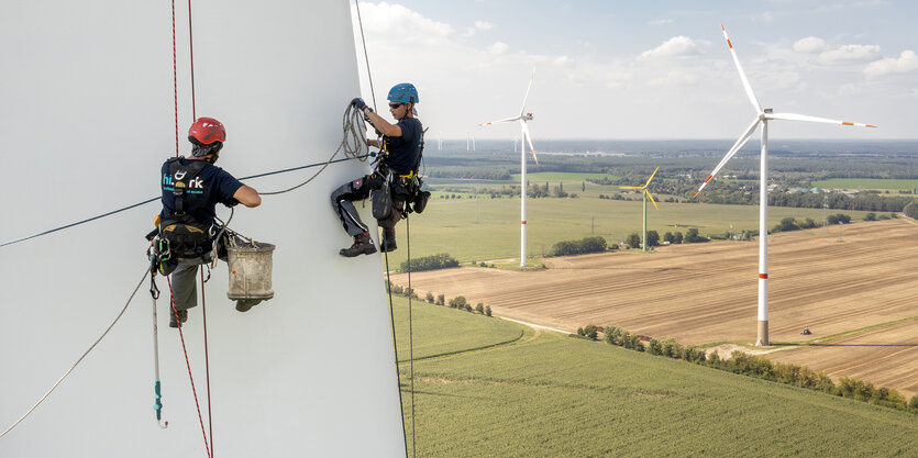 Industriekletterer beim Arbeiten am 55 Meter langen Rotorblatt einer Windkraftanlage, im Hintergrund sind in der Landschaft weitere Windkraftanlagen zu sehen