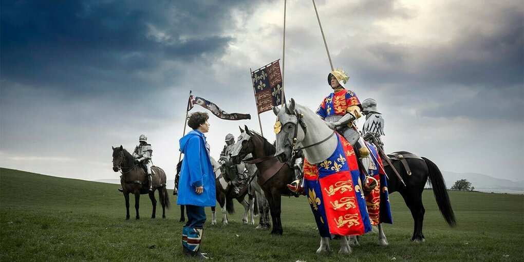 Eine Frau unterhält sich auf einem Feld mit Menschen in Kostümen, die auf Pferden sitzen