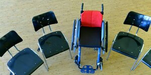 Ein Rollstuhl steht in einer Schule zwischen anderen Stühlen.