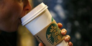 Ein Mensch trinkt aus einem Starbucks to-go Becher