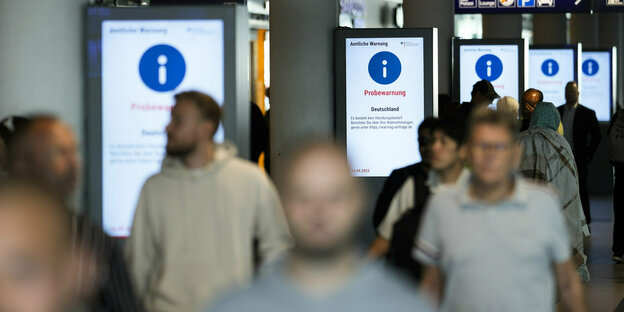Menschen laufen durch den Hauptbahnhof Berlin und werden über den Probealarm informiert