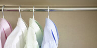 Vier Hemden hängen frisch gebügelt auf Kleiderbügeln im Schrank