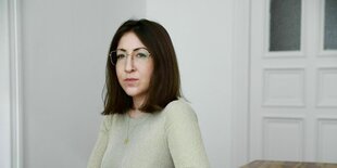 Deborah Feldman sitzt mit einem hellen Pulli an eiem leeren Küchentisch und schaut skeptisch in die Kamera