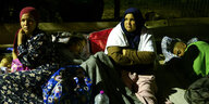 Zwei Frauen mit ihren schlafenden Kindern sitzen auf dem Boden und schauen besorgt in die Kamera