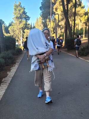 Shira Ben Sasson, mit Kopftuch und Snaekers bekleidet, trägt eine mit einem Tuch bedeckte Torarolla